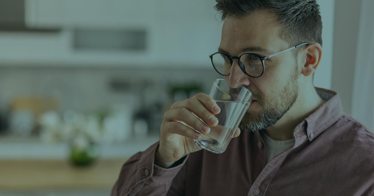 Man in kitchen drinking a glass of water.